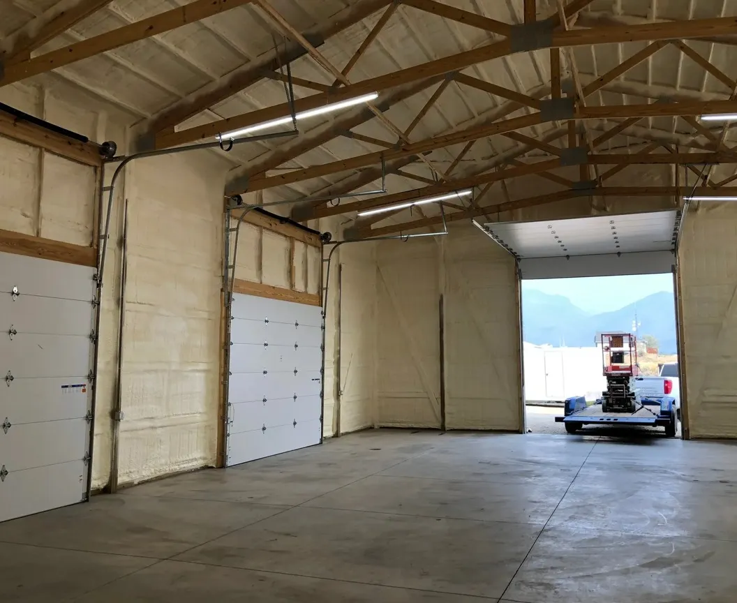 Insulated warehouse interior with open garage door, lift on a trailer outside, and fluorescent lighting.