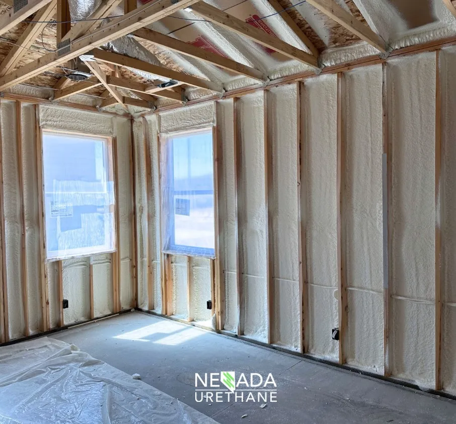 Partially insulated room with wooden framing and spray foam, covered floor.